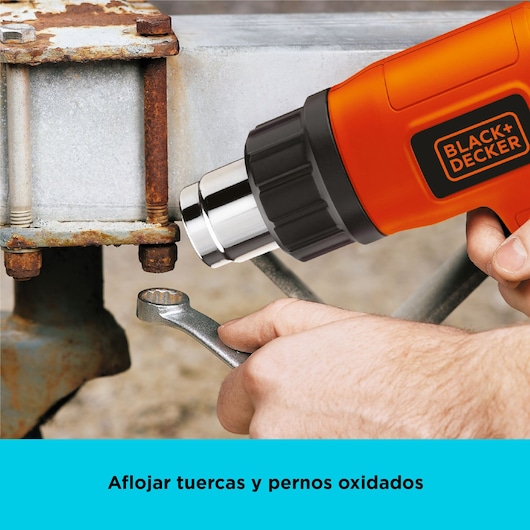 Close-up of BLACK+DECKER HG1500 heat gun loosening rusted bolts on metal with wrench, product in use.