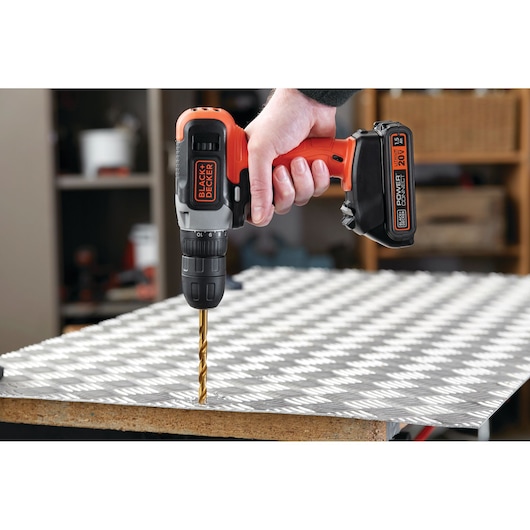 BLACK+DECKER BCD702C1 cordless drill in use drilling metal sheet, orange and black design, close-up side view.