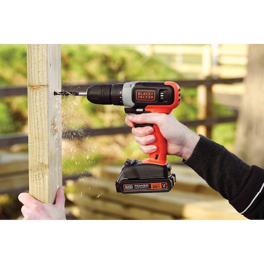 BLACKDECKER BCD702C1 cordless drill in use, drilling into wood outdoors.