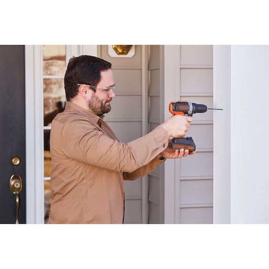 BLACKDECKER cordless drill BCD703C1 used on exterior wall, side view, orange and black design.