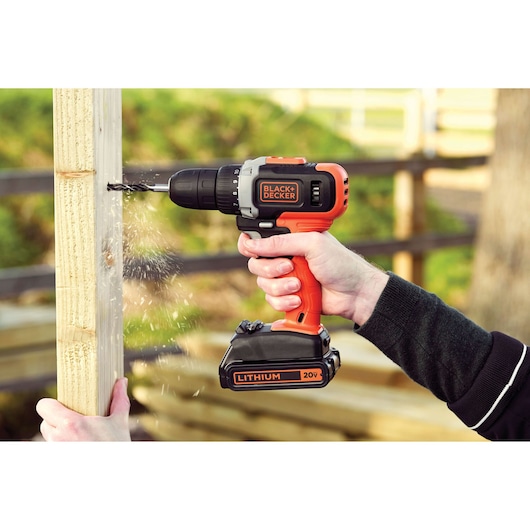BLACK+DECKER BCD703C1 cordless drill in use drilling wood outdoors, orange and black design, photography.