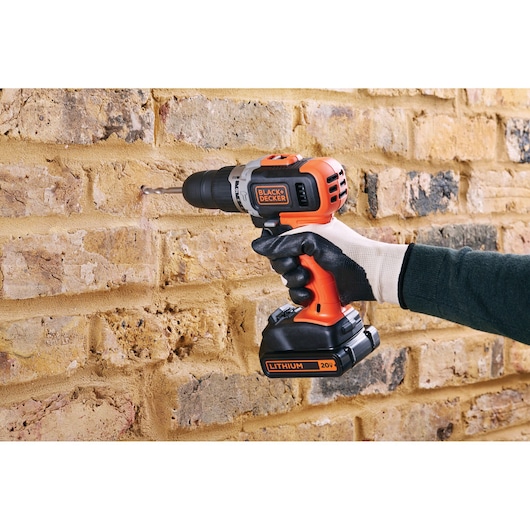 BLACKDECKER BCK21S1S cordless drill used on a brick wall, orange and black, 20V lithium battery.