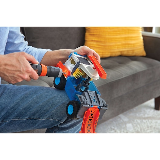 Photo of person using BLACKDECKER BCF601AA cordless screwdriver to assemble a colorful toy truck indoors.