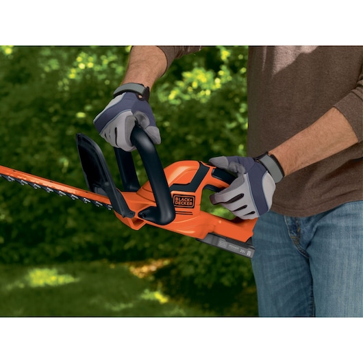 BLACKDECKER BCHT222D1 hedge trimmer in use, orange and black body, person wearing gloves outdoors.