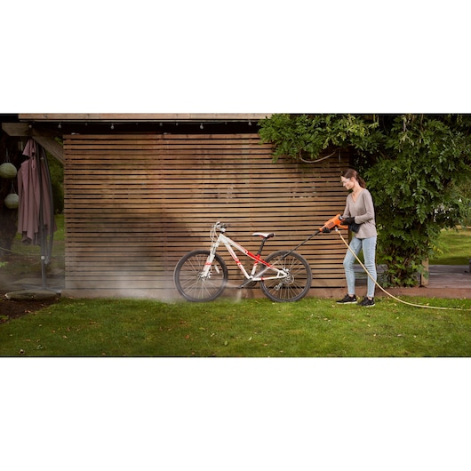 BLACKDECKER BCPC20D1 pressure washer cleaning a white and red bicycle outdoors on grass.