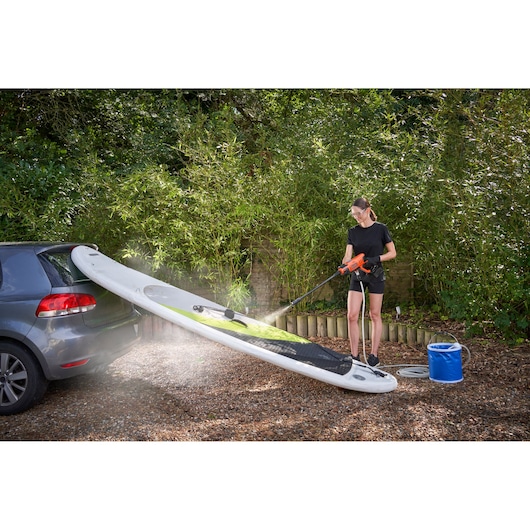 BLACKDECKER BCPW350E1 portable pressure washer cleaning a paddleboard near a car outdoors.