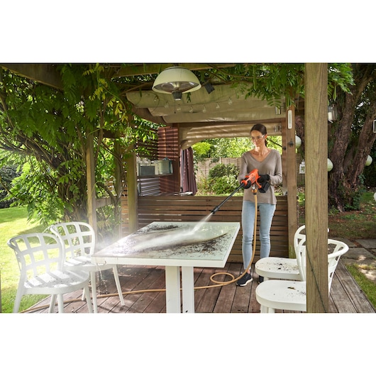 Photo of person cleaning outdoor table with BLACKDECKER BCPW350E1 pressure washer, in a garden patio setting.