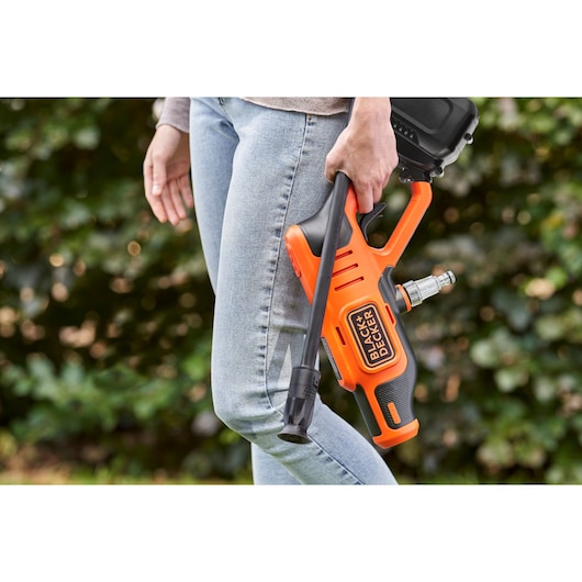 Photo of a person holding a BLACKDECKER BCPW350E1 cordless power washer, orange and black, outdoors.