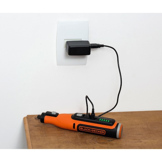 Photo of BLACK+DECKER BCRT8K35 cordless screwdriver charging with cable connected to wall outlet, tool on wooden surface.