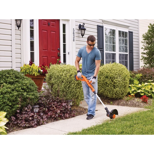 Photo of person using BLACKDECKER BCST201C1 cordless string trimmer on garden sidewalk.