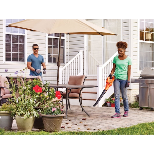 Photo of a person using BLACKDECKER BCSW221E1 cordless sweeper on a patio with outdoor furniture and plants.