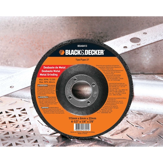 A BLACK+DECKER metal grinding disc, type 27, model BDA0413, with an orange and black label showing usage for metal grinding. The disc is 115mm x 6mm x 22mm (4-1/2'' x 1/4'' x 7/8'') and is placed on a metal surface.