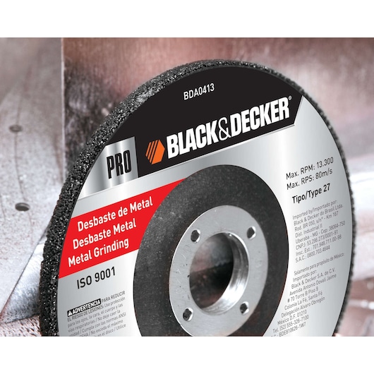 Close-up image of a BLACK+DECKER metal grinding disc, model BDA0413, with specifications printed on the label. The disc shows the brand name, 'PRO,' and is labeled for metal grinding. There are details about maximum RPM, RPS, and type 27. The disc is attached to a piece of metal machinery.