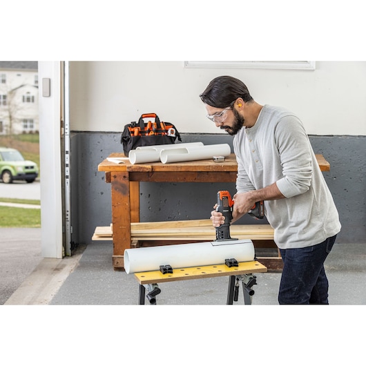 BLACKDECKER BDCDMT1206KITC cordless tool kit in use, person cutting PVC pipe in workshop setting.