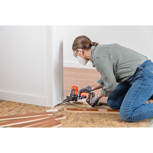 Person using BLACKDECKER BDCDMT1206KITC cordless multi-tool to cut flooring near a doorway during installation.