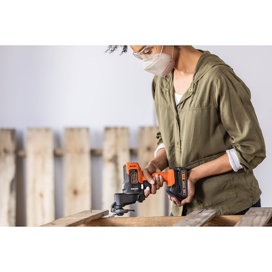 Person using BLACKDECKER BDCDMT1206KITC cordless multi-tool on wood pallet, orange and black power tool visible.