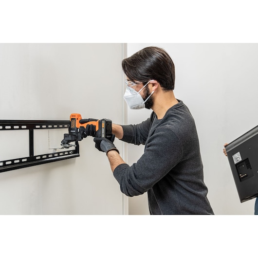 BLACKDECKER BDCDMT1206KITC cordless drill in use mounting a TV bracket to a wall, user wearing gloves.