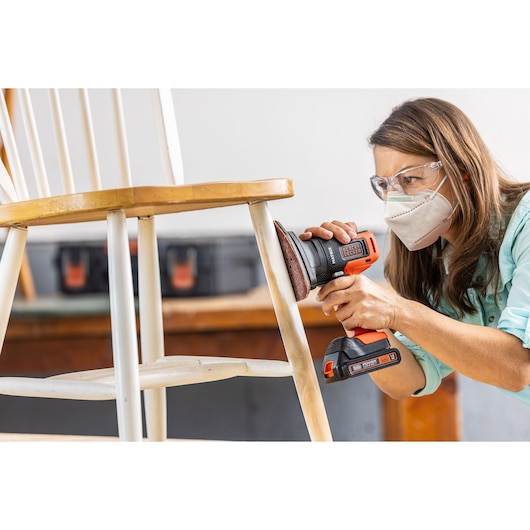BLACKDECKER BDCDMT1206KITC cordless drill with sander attachment used on white wooden chair, close-up.
