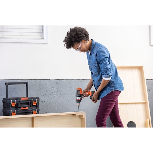 Photo of person using BLACKDECKER BDCDMT1206KITC cordless drill on wooden furniture, toolboxes in background.