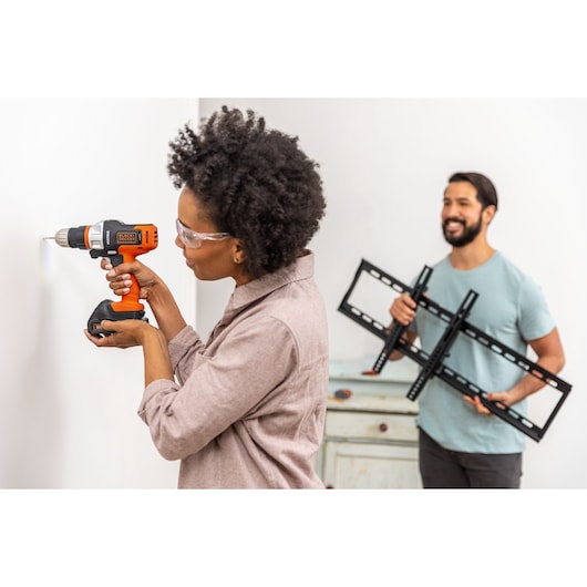 Photo of person using BLACKDECKER cordless drill BDCDMT1206KITC to drill into a wall, another holding TV mount.