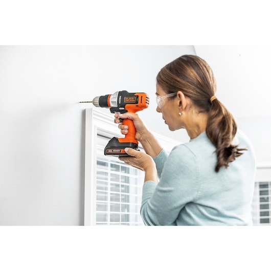 Photo of a person using a BLACK+DECKER BDCDMT1206KITC cordless drill on a white indoor wall.