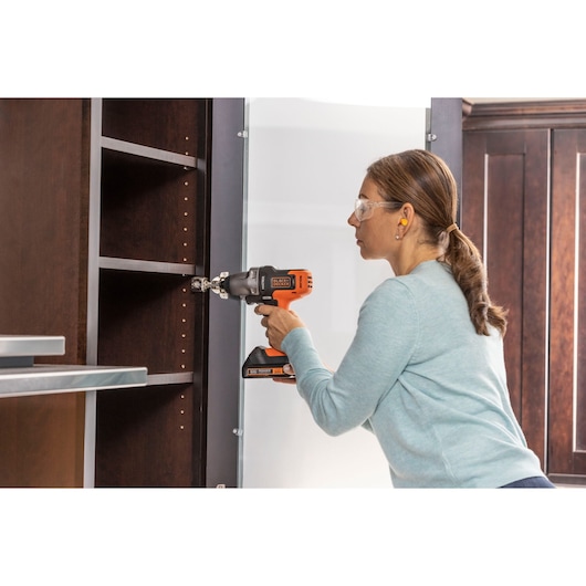 Photo of a person using a BLACKDECKER BDCDMT1206KITC cordless drill on a dark wood cabinet.