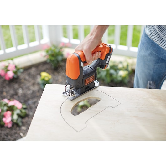 Photo of BLACK+DECKER BDCK502C1 jigsaw cutting a curved shape into plywood, handheld in outdoor setting.