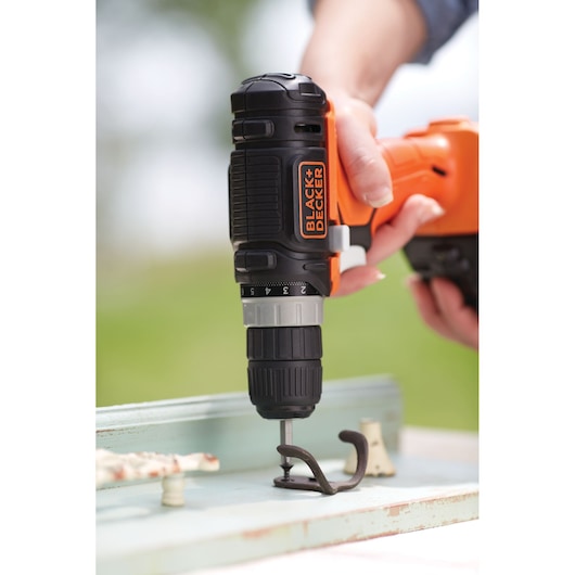 Photo of BLACK+DECKER BDCK502C1 cordless drill in use mounting a metal hook onto a wood surface.