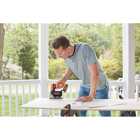 BLACKDECKER BDCK502C1 cordless jigsaw in use cutting wood outdoors on a sawhorse worktable.