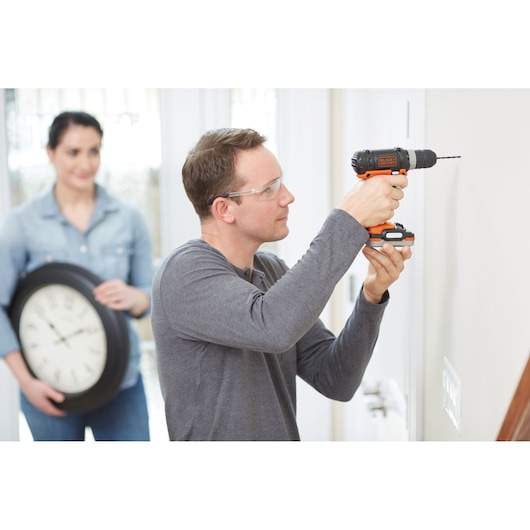 Photo of BLACKDECKER BDCK502C1 cordless drill in use to drill into a wall, person holding a large clock in background.