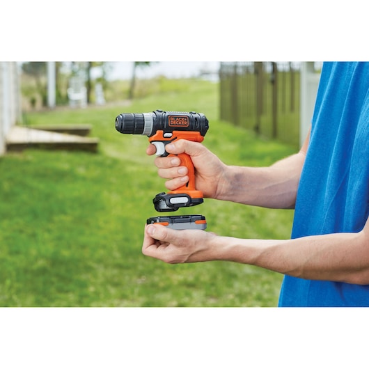 Photo of BLACK+DECKER cordless drill BDCK502C1 held by a person outdoors, with battery pack being attached.