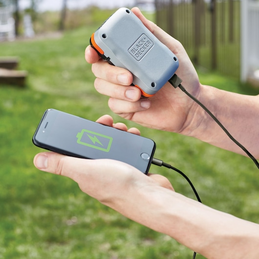 BLACK+DECKER BDCK502C1 portable charger charging a smartphone outdoors using a USB cable.