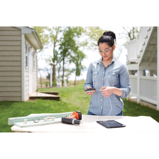 BLACKDECKER BDCK502C1 cordless drill and accessories on outdoor table with person charging device, side angle.