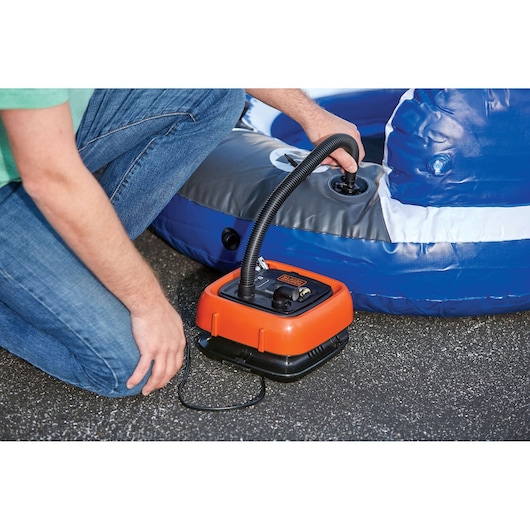BLACKDECKER BDINF12 orange inflator pumping air into a blue inflatable on asphalt, close-up.