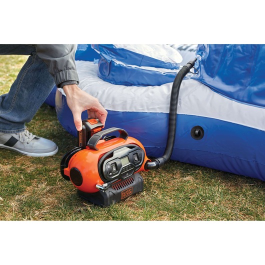 Photo of BLACKDECKER BDINF20 orange portable air inflator in use inflating a blue and white pool outdoors.