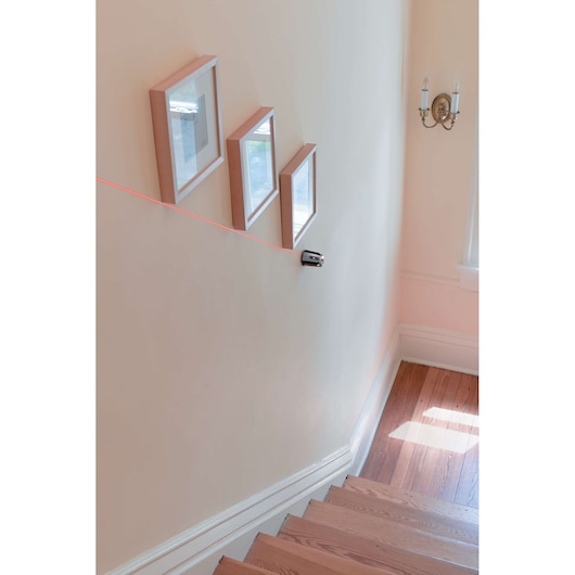 BLACKDECKER BDL220S laser level projecting red line on stairway wall with picture frames for alignment.