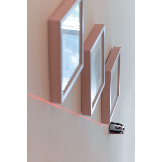 BLACKDECKER BDL220S laser level projects a red line on wall, aligning picture frames, side view.