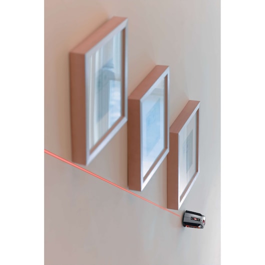 Photo of BLACKDECKER BDL220S laser level on wall projecting red line under picture frames, side angle.