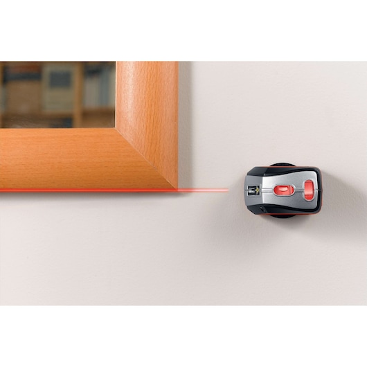 BLACKDECKER BDL220S laser level projecting a red horizontal line on a wall next to a wooden frame, top-down angle.
