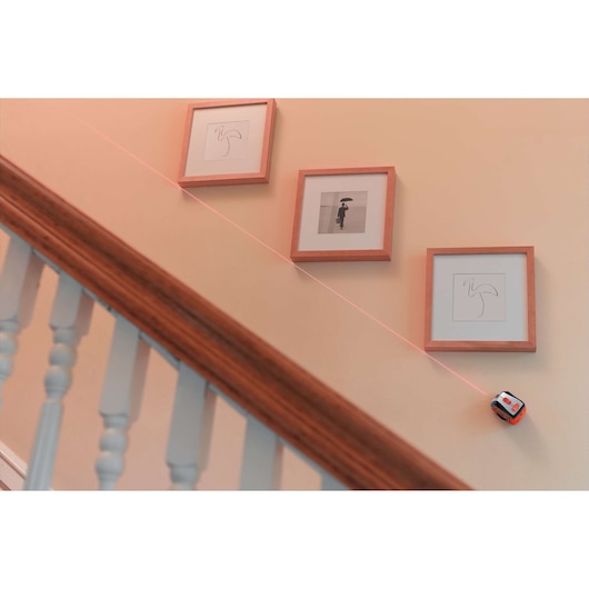 BLACKDECKER BDL220S laser level on staircase wall projects straight red line beneath framed pictures.