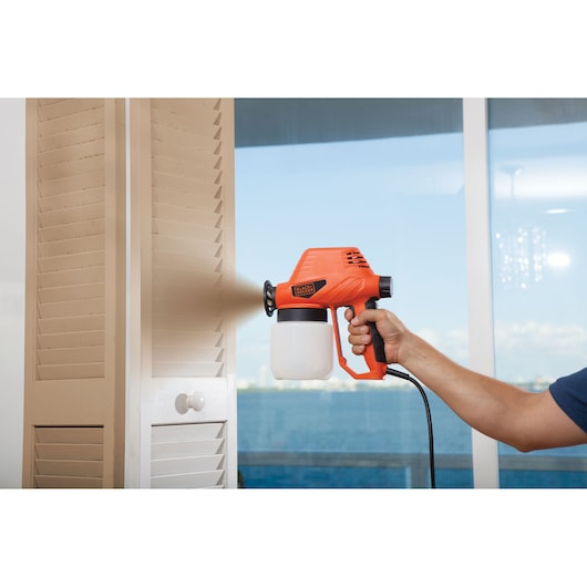 Photo of BLACKDECKER BDPS130 paint sprayer in use painting a beige cabinet near a window.