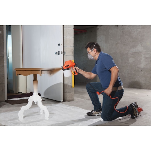BLACKDECKER BDPS130 paint sprayer used to paint a wooden table in a workshop setting.