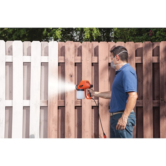 BLACKDECKER BDPS130 paint sprayer used to paint wooden fence outdoors.