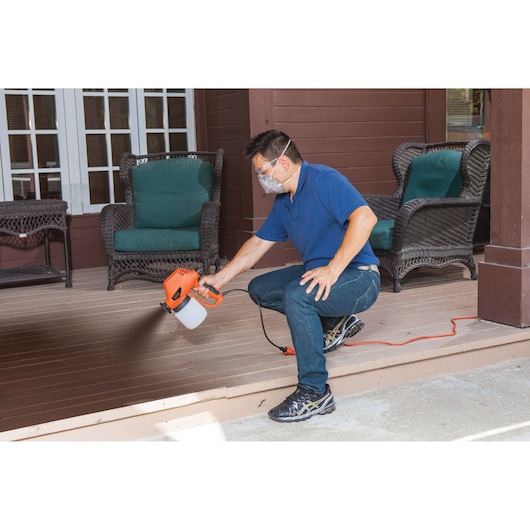 BLACKDECKER BDPS130 handheld paint sprayer used for staining wooden porch in outdoor setting.