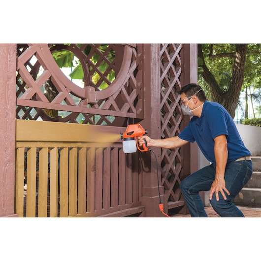 BLACKDECKER BDPS130 paint sprayer used outdoors to paint brown wooden fence.