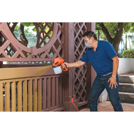 BLACKDECKER BDPS130 paint sprayer used to paint brown outdoor wooden fence.