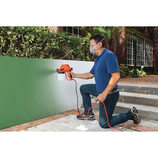 Person uses BLACKDECKER BDPS130 paint sprayer to paint an outdoor wall green.