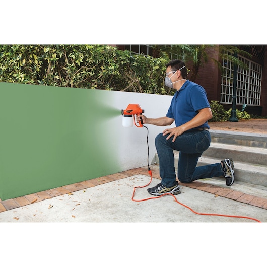 BLACKDECKER BDPS130 paint sprayer in use, spraying green paint on outdoor wall.