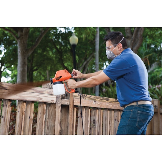 BLACKDECKER BDPS130 paint sprayer used on wooden fence outdoors.