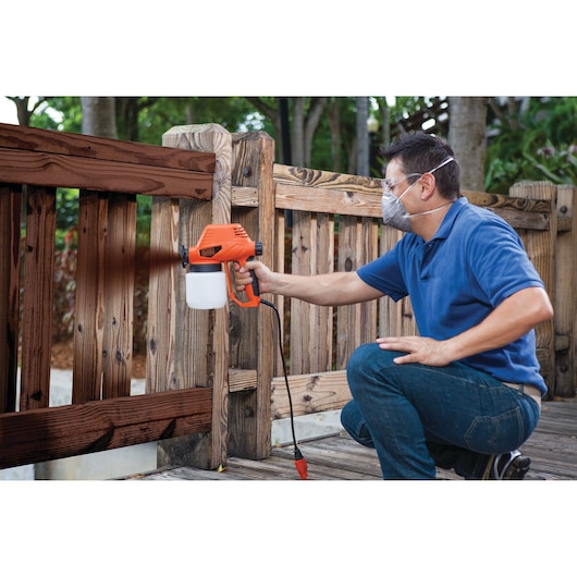 BLACKDECKER BDPS130 paint sprayer used outdoors for staining a wooden fence.